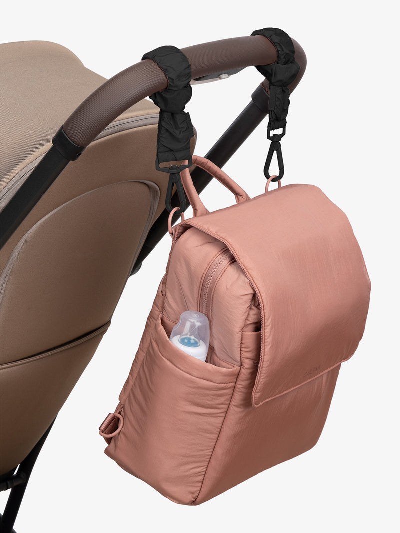 CALPAK Convertible Mini Diaper Backpack in pink Peony with Black Stroller Straps attached to a brown stroller