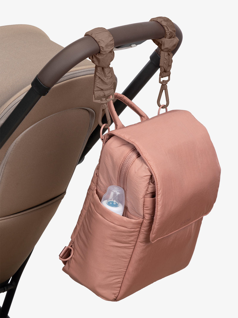 CALPAK Convertible Mini Diaper Backpack in pink Peony with brown Hazelnut Stroller Straps attached to a brown stroller