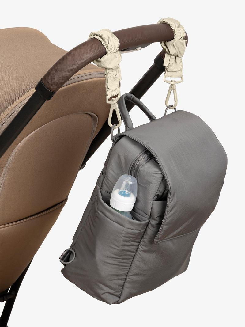 CALPAK Convertible Mini Diaper Backpack in grey Slate with white Oatmeal Stroller Straps attached to a brown stroller