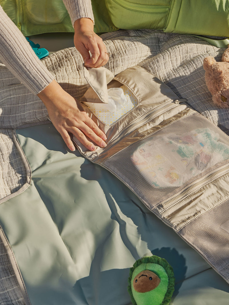 Model displaying designated baby wipe pocket of CALPAK Portable Changing Pad Clutch in oatmeal