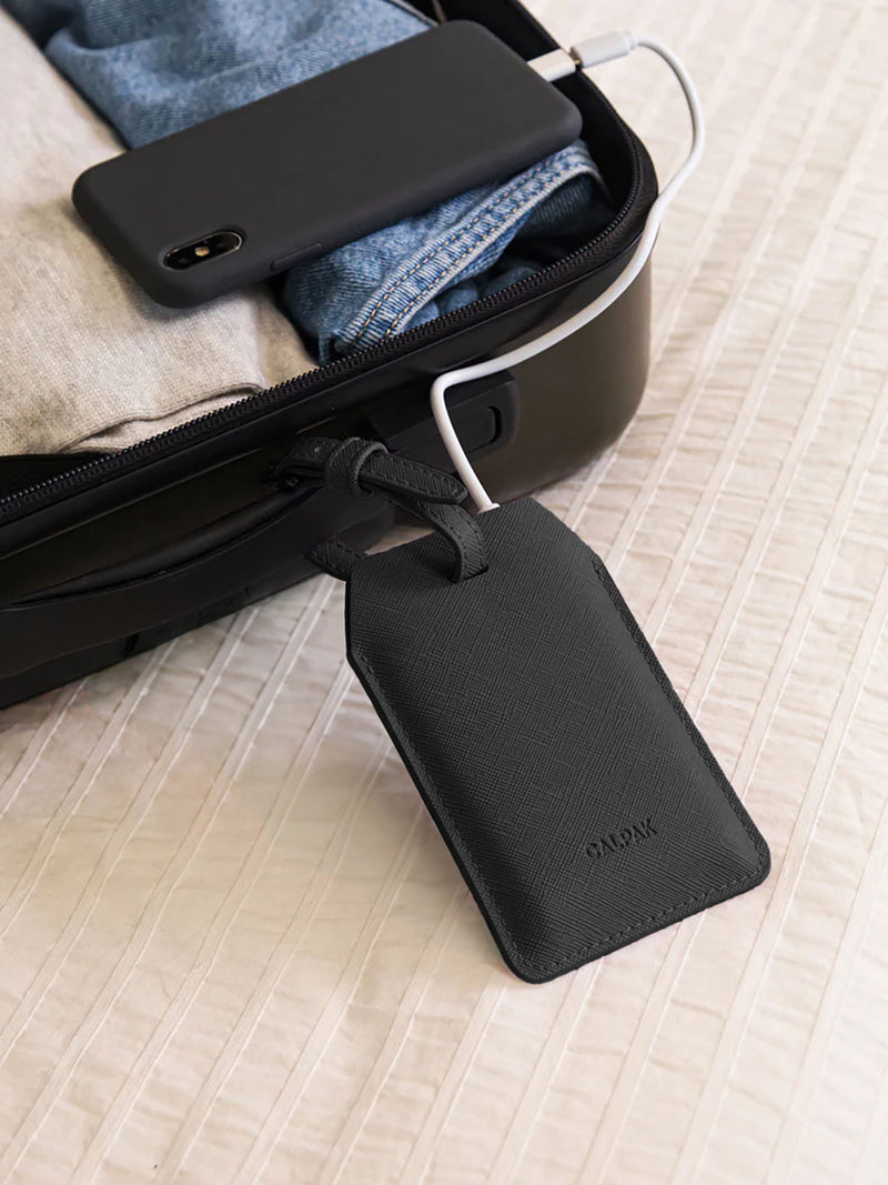 CALPAK Portable Luggage Tag + Charger attached to handle of suitcase with iPhone charging by lightning cord