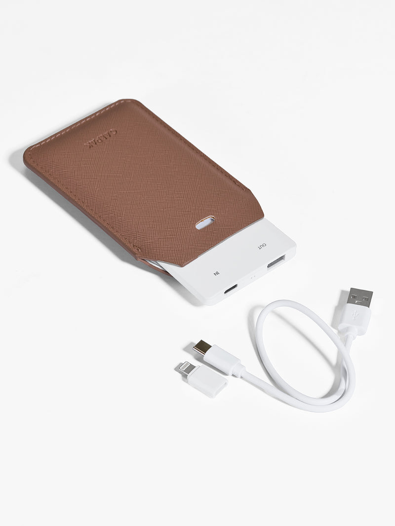 Caramel brown CALPAK Portable Luggage Tag + Charger featuring included cord, USB-C and Lighting adaptor compatibility and 2500 mAh battery power