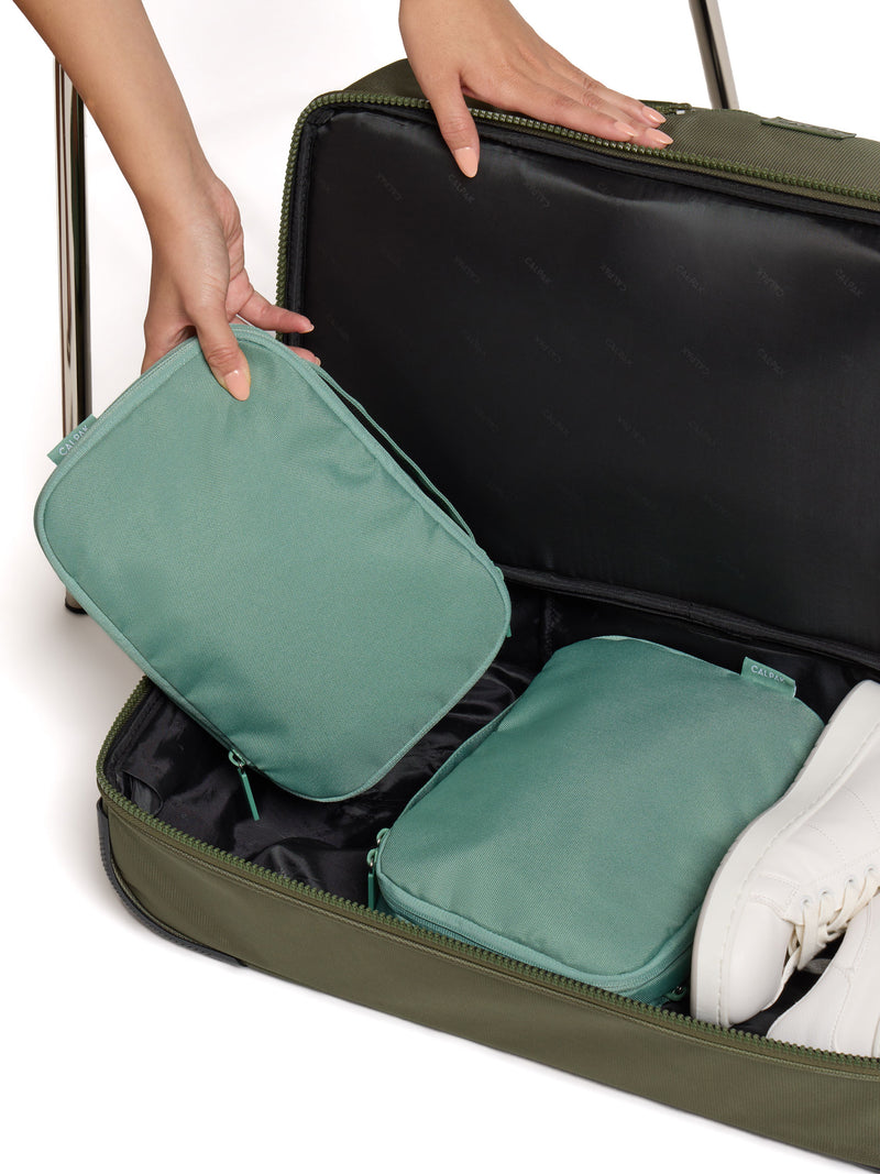 Model placing sage green CALPAK small compression packing cube within bottom compartment of Stevyn Duffel Bag