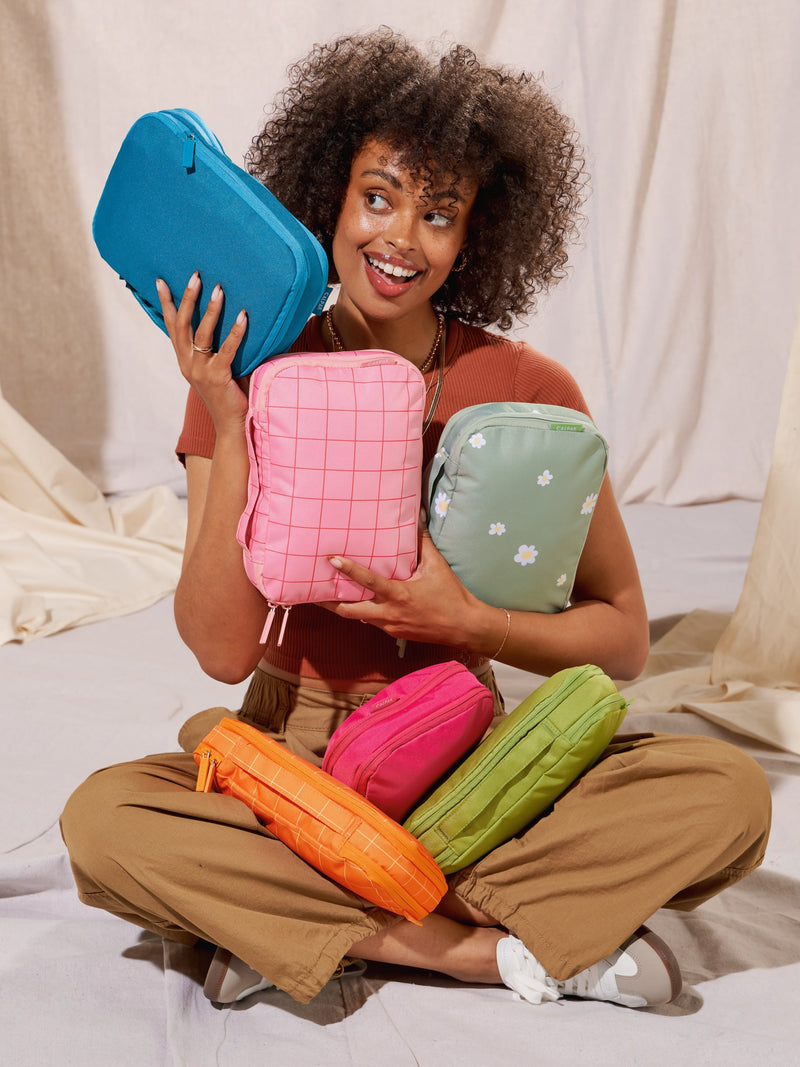 Model displaying CALPAK Small Compression Cubes in daisy, pink grid, lagoon, orange grid, dragonfruit, and palm