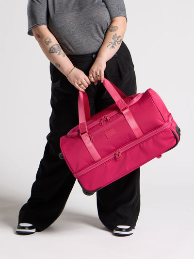 CALPAK Stevyn Rolling Duffel side view with top handle extended in hot pink dragonfruit; DSR2201-DRAGONFRUIT view 2