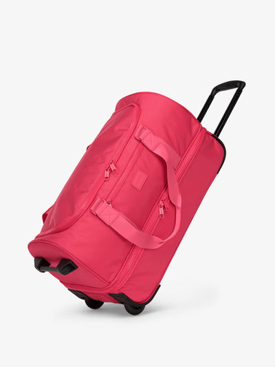 CALPAK Stevyn Rolling Duffel side view with top handle extended in hot pink dragonfruit; DSR2201-DRAGONFRUIT view 1