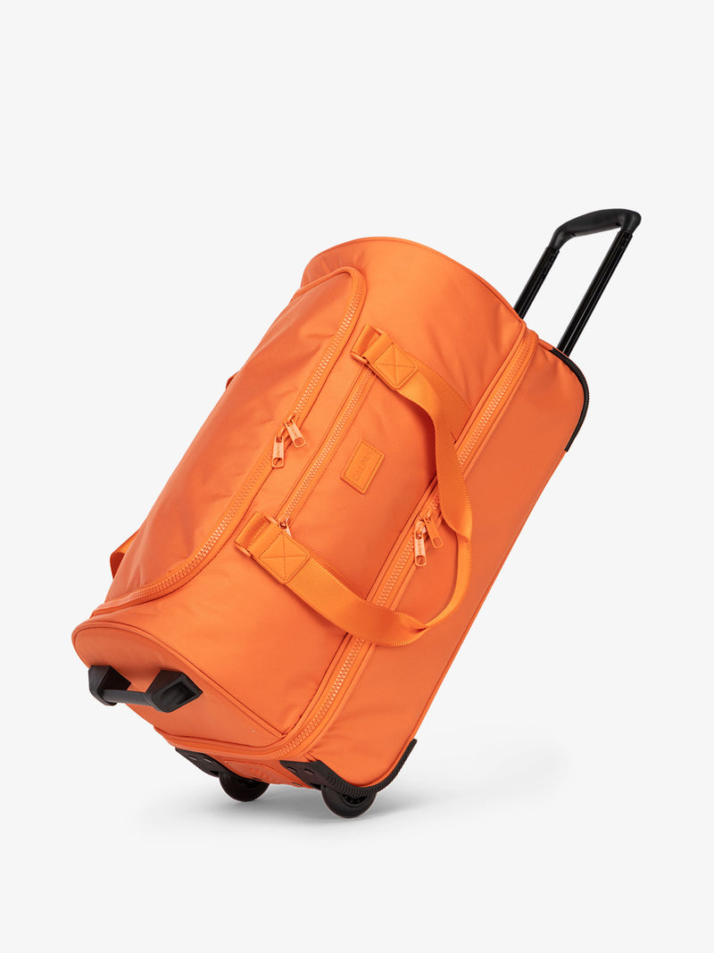 CALPAK Stevyn Rolling Duffel side view with top handle extended in orange