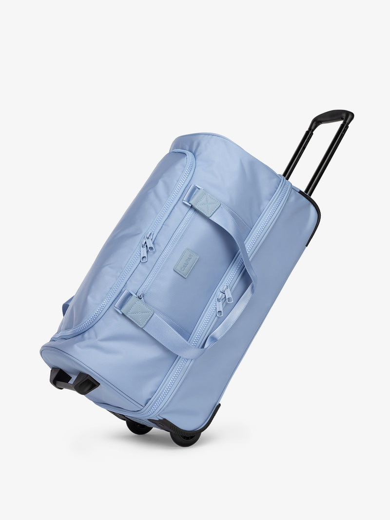 CALPAK Stevyn Rolling Duffel side view with top handle extended in sky