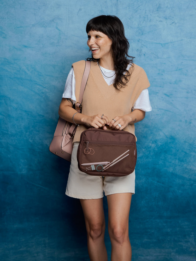 Model standing against wall with CALPAK Tablet Tech Organizer in walnut and CALPAK Kaya Laptop Backpack