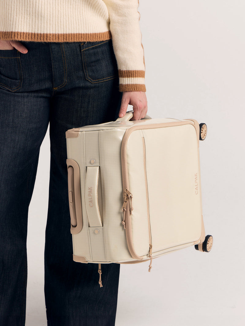 Model holding CALPAK Terra 35L Soft Sided Carry-On Luggage in White Sands by the side handle