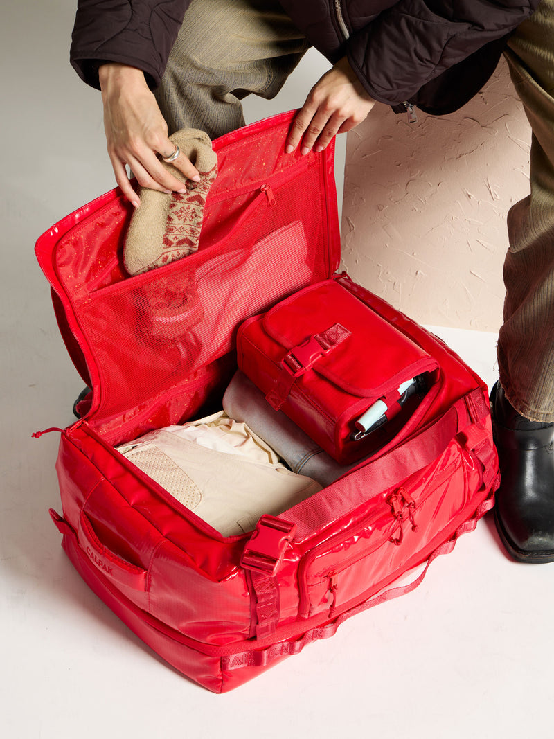 Model placing socks into mesh interior pocket of CALPAK Terra Large 50L Duffel Backpack in red; DTL2301-FLAME