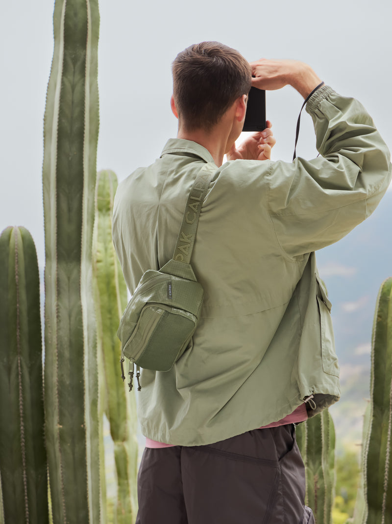 Model wearing CALPAK Terra crossbody belt bag with adjustable strap and water resistant exterior in juniper