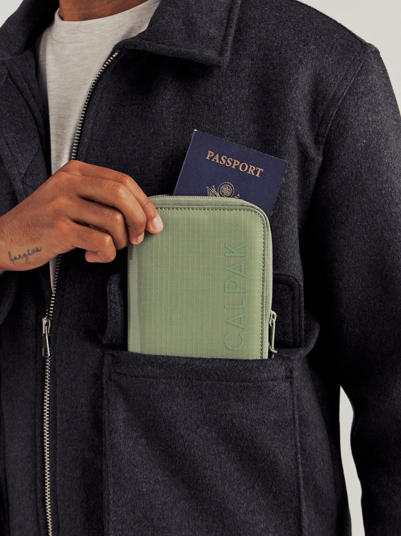 CALPAK Terra Zippered Passport Wallet in Juniper with passport being placed inside a model's jacket pocket