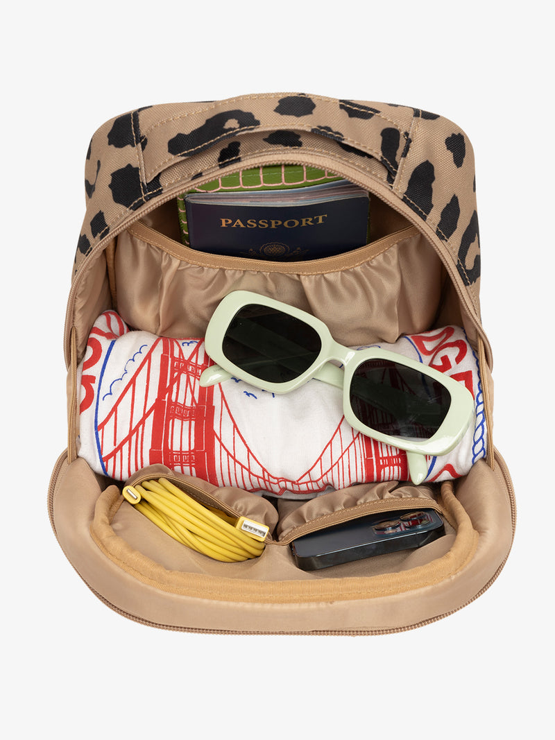 Interior view of cheetah CALPAK The Everything Cube with notebook and passport in large slip pocket, cords and phone in front slip pockets, and sunglasses and t-shirt in main compartment