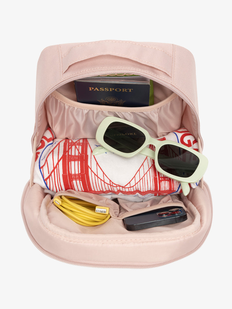 Interior view of pink sand CALPAK The Everything Cube with notebook and passport in large slip pocket, cords and phone in front slip pockets, and sunglasses and t-shirt in main compartment