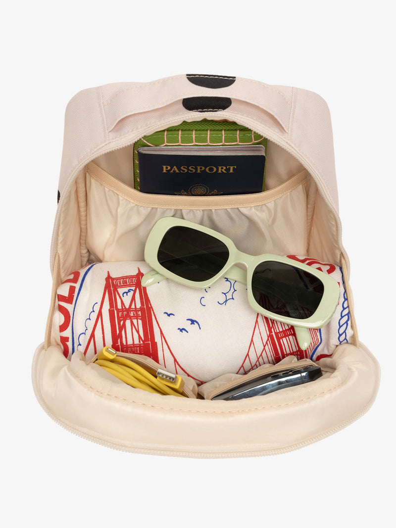 Interior view of polka dot CALPAK The Everything Cube with notebook and passport in large slip pocket, cords and phone in front slip pockets, and sunglasses and t-shirt in main compartment