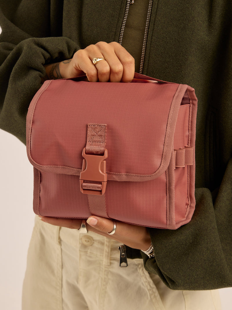 Model holding the CALPAK Terra Hanging Toiletry Bag in red and orange Matte Clay