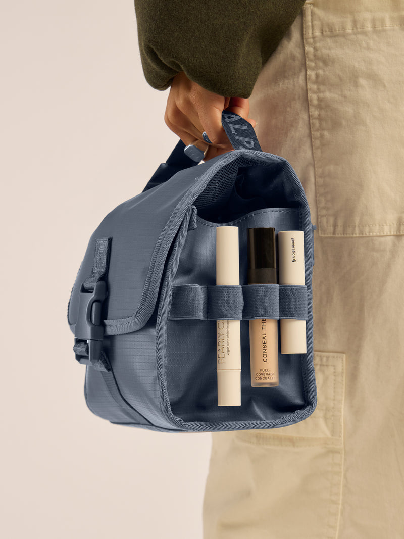 Model holding the CALPAK Terra Hanging Toiletry Bag in blue Matte Indigo