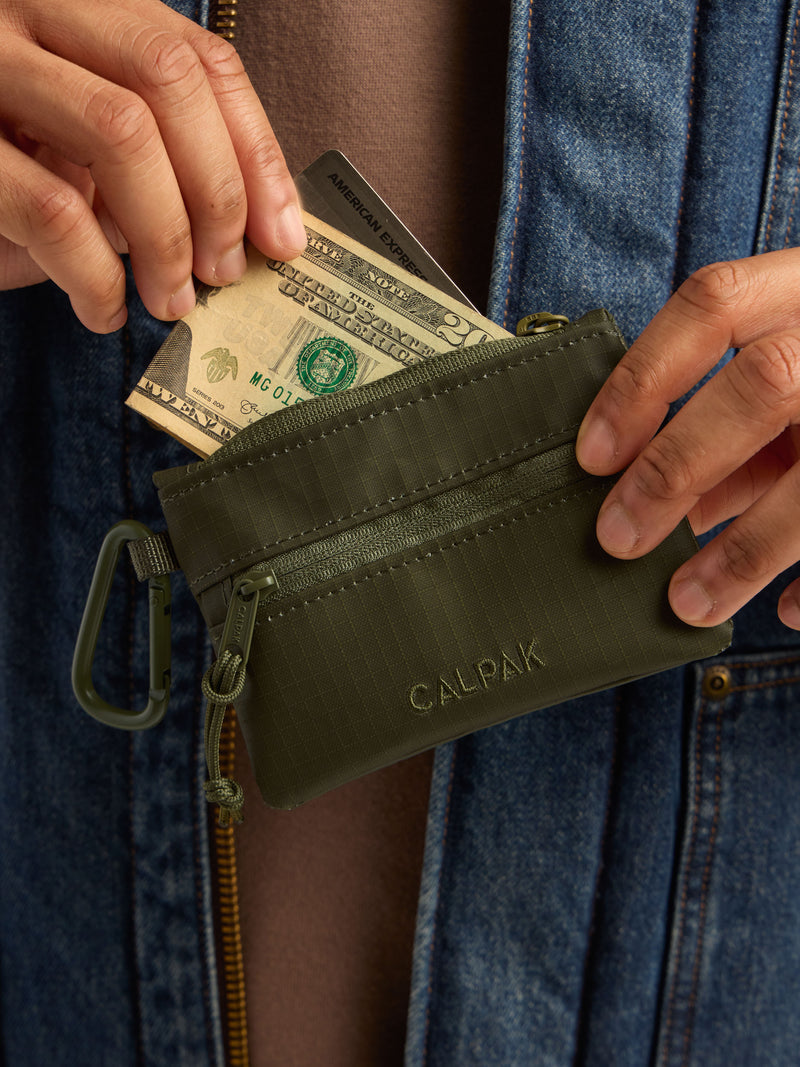 Model adding money in the CALPAK Terra Clippable Card Pouch in dark green Matte Pine front view