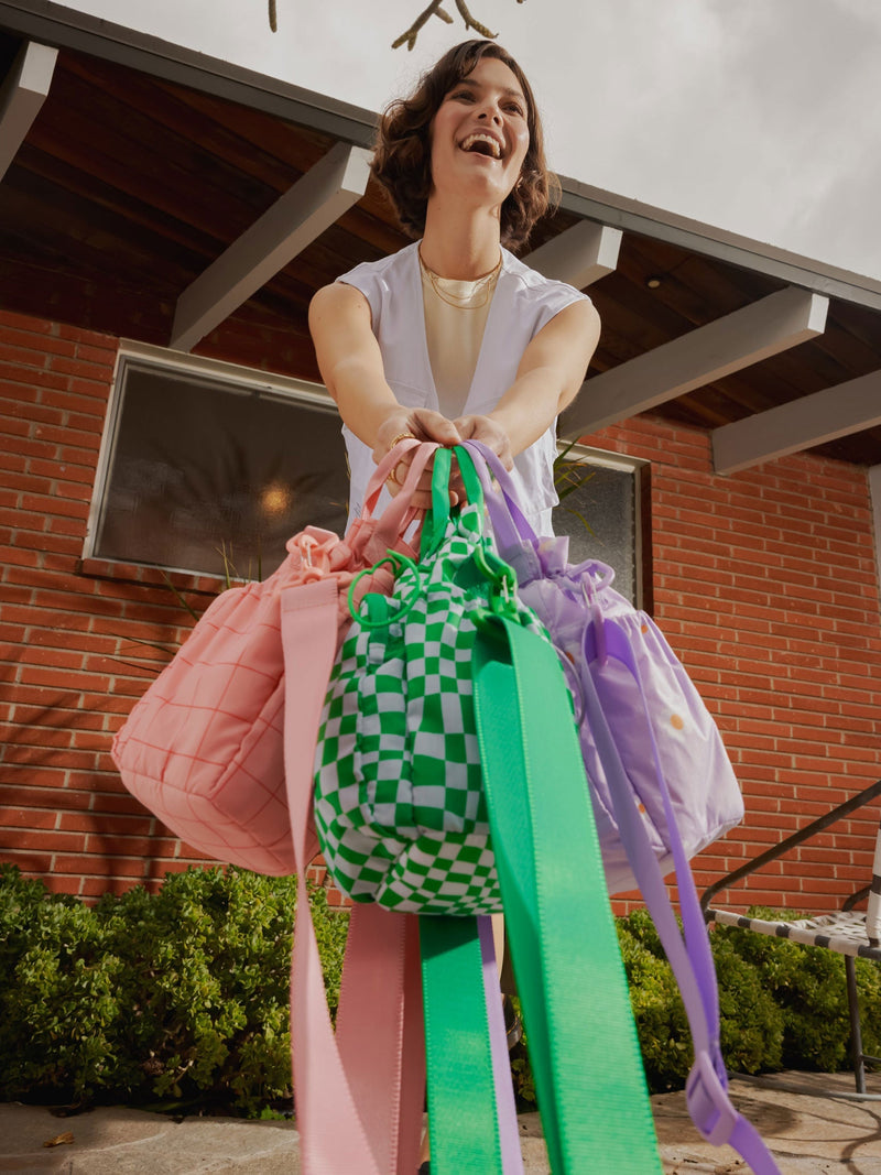 Model carrying CALPAK Water Bottle Holders with detachable sling, top handles and zipped front pocket in pink grid, green checkerboard and purple floral print