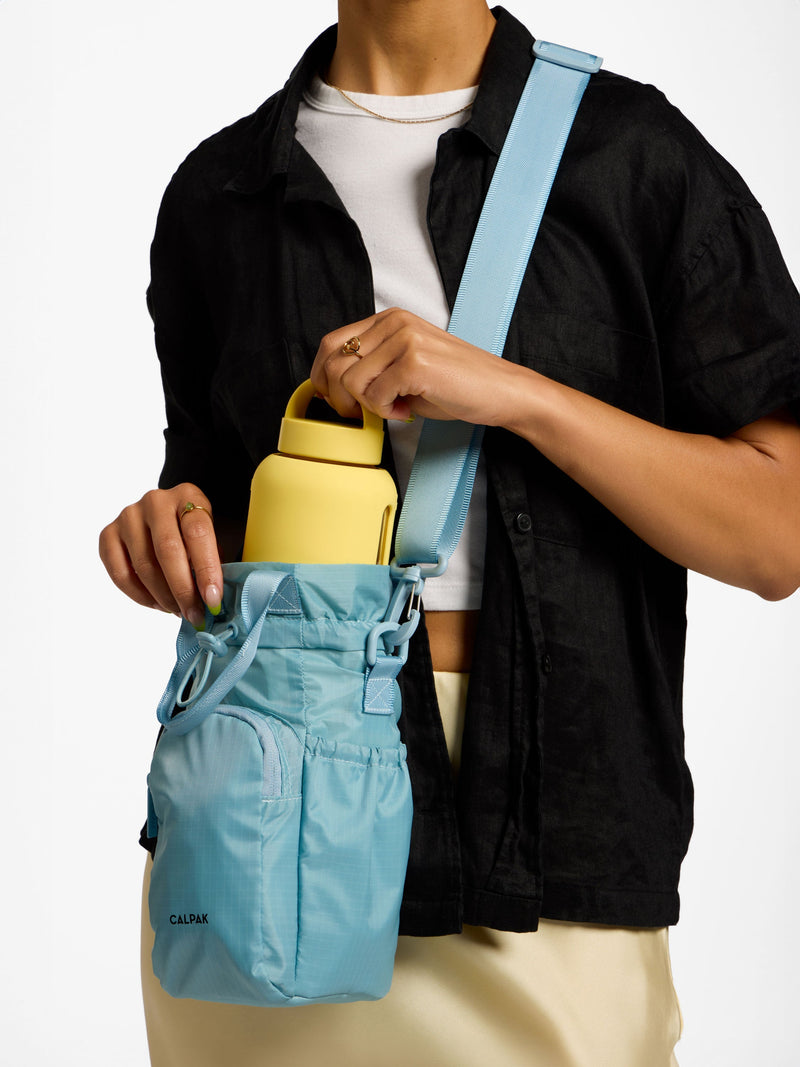 Model wearing CALPAK Water Bottle Holder with crossbody strap in powder blue