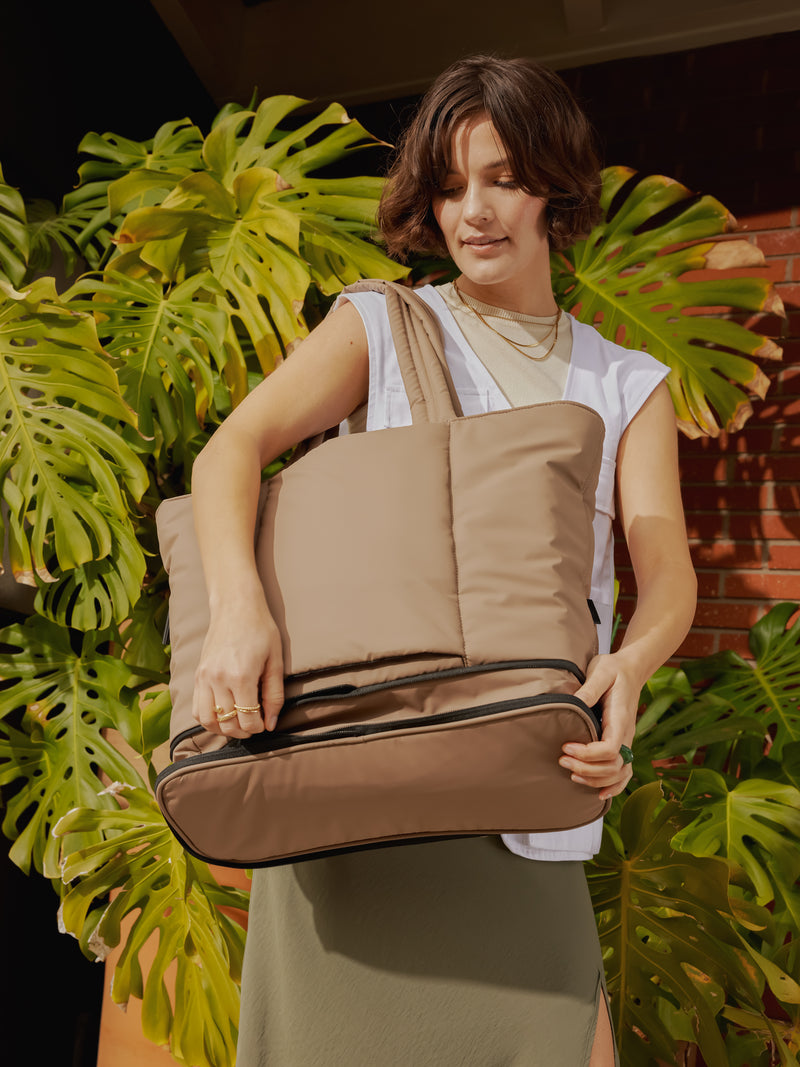 Model carrying CALPAK Luka expandable travel bag with laptop compartment in chocolate